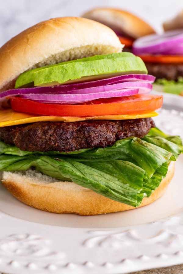 Hamburger topped with lettuce, cheese, tomato, red onion and avocado on a bun, ready to eat.