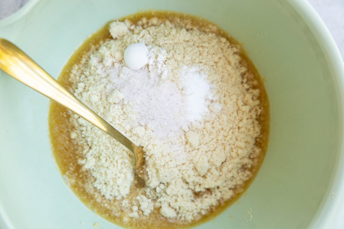 Dry ingredients on top of wet ingredients in a mixing bowl to make almond flour blueberry cookies.