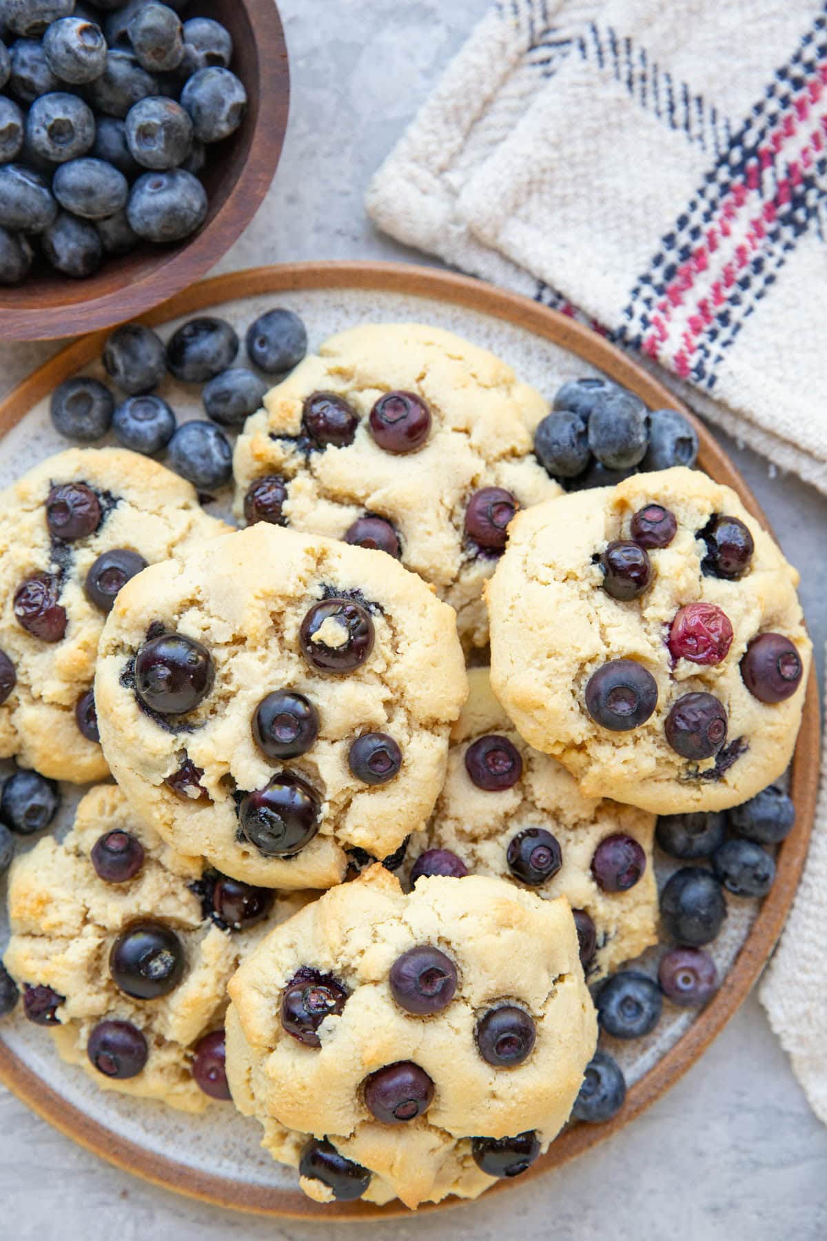 Plate of almond flour blueberry cookies with a bowl of fresh berries to the side.