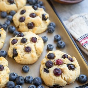 Baking sheet with blueberry almond flour cookies and fresh blueberries everywhere.