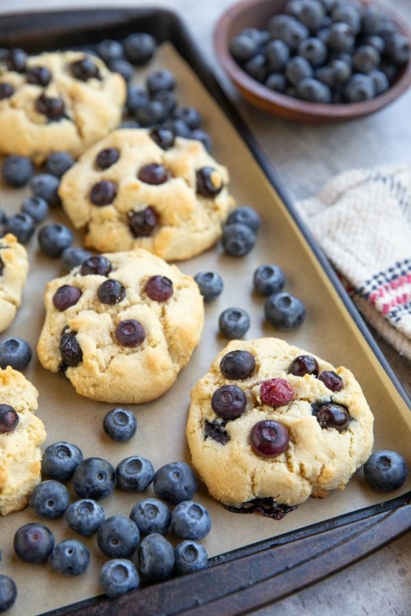 Baking sheet with blueberry almond flour cookies and fresh blueberries everywhere.