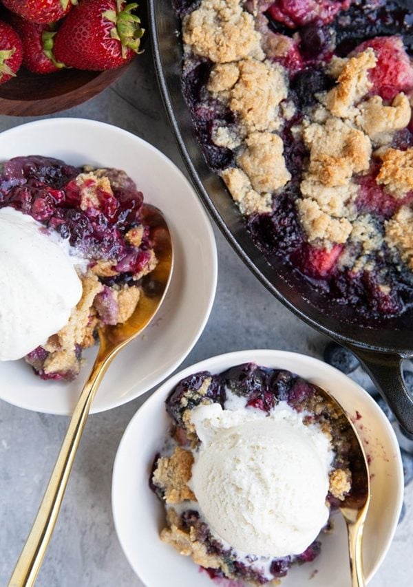 Two bowls and a dish of mixed berry cobbler with scoops of ice cream in the bowls.