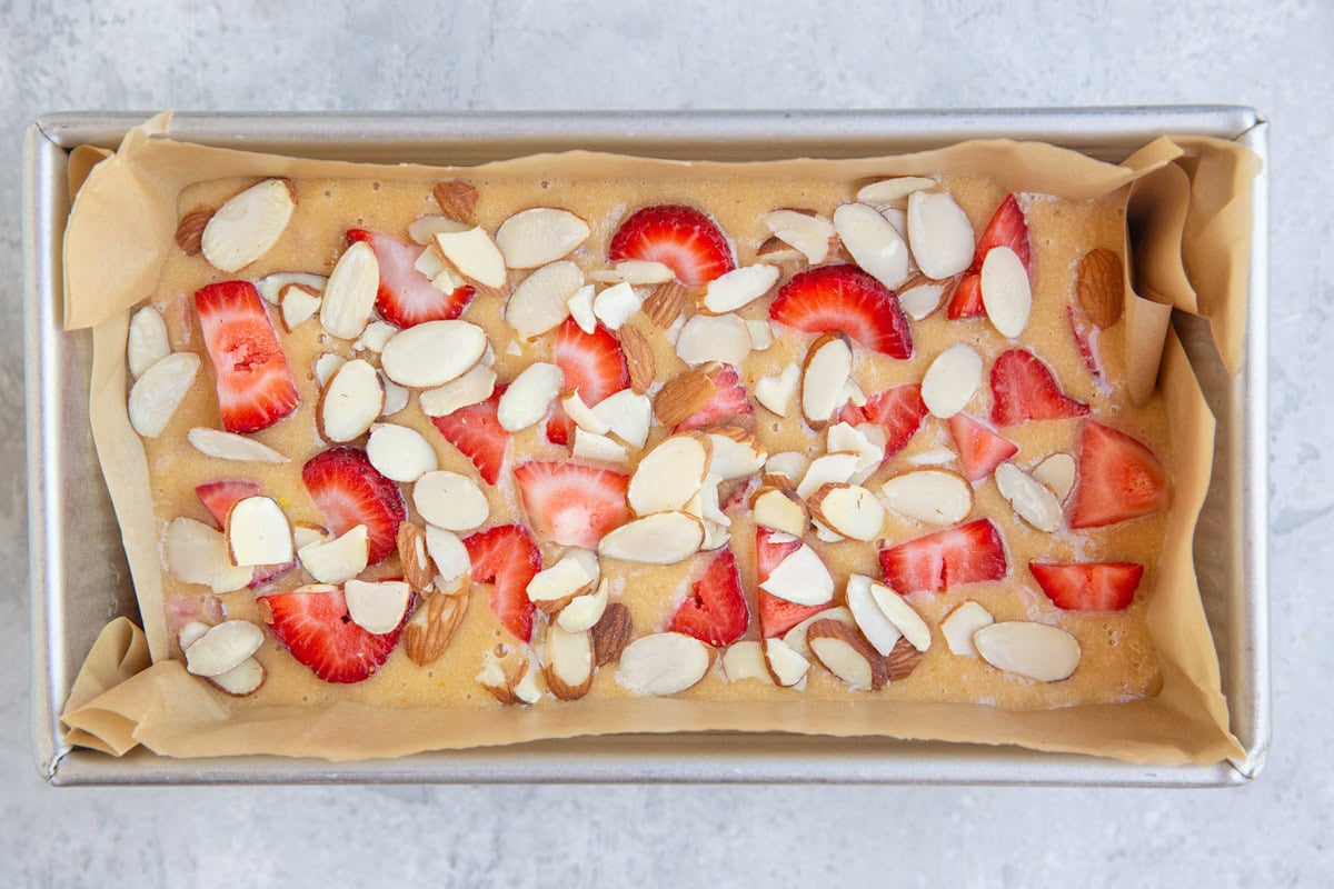 Loaf pan with almond flour quick bread batter inside with fresh strawberries and sliced almonds.