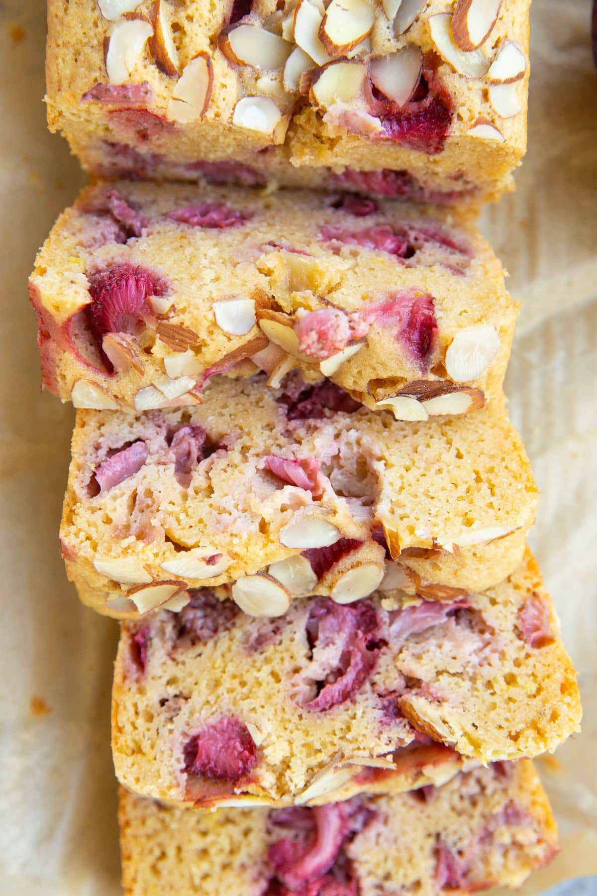 Loaf of strawberry bread on parchment paper cut into slices, ready to eat.