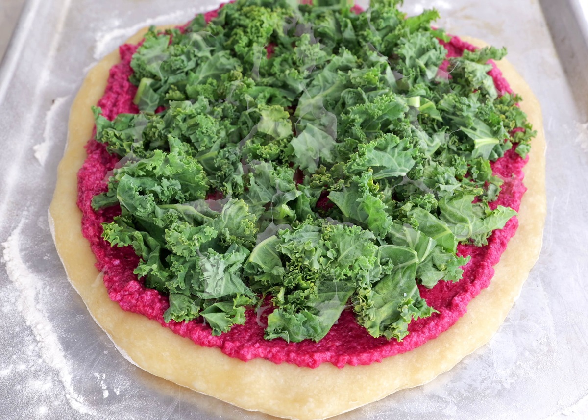 Pizza crust with beet pesto and chopped kale on top.