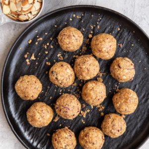 Cranberry Almond Protein Balls on a black plate with a bowl of dried cranberries and almonds to the side.