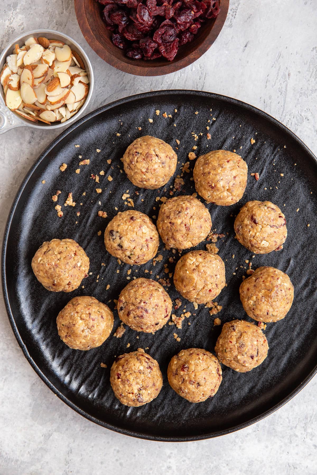 Cranberry Almond Protein Balls on a black plate with a bowl of dried cranberries and almonds to the side.