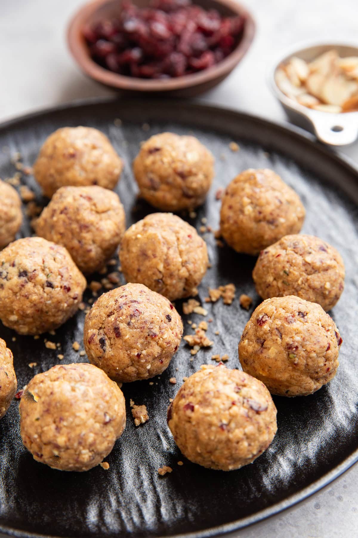 Cranberry almond protein bites on a black plate with a bowl of dried cranberries in the background.