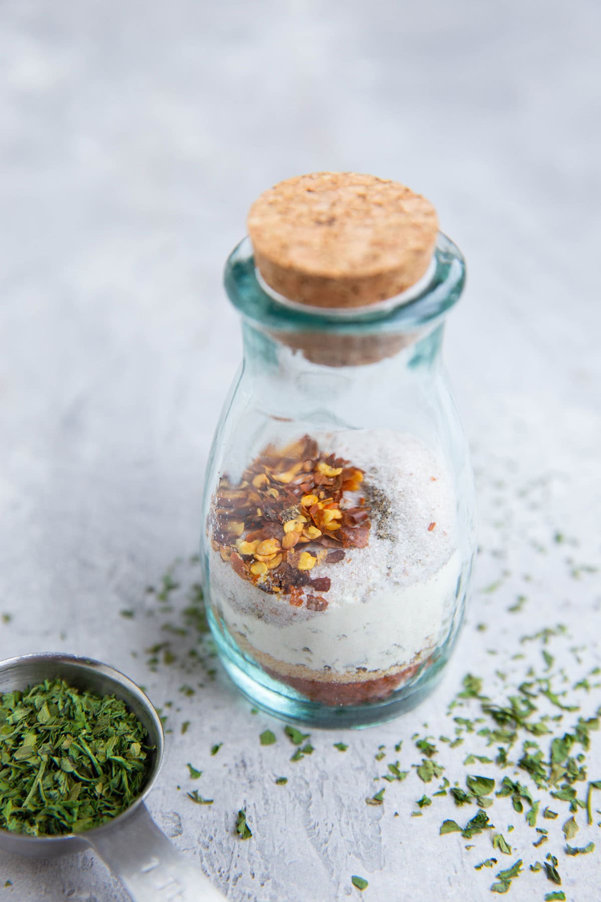 Dry rub for beef in a small glass jar with a top on it. Dried oregano to the side.