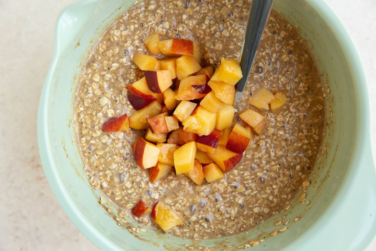 Peaches on top of oatmeal muffin mixture, ready to be mixed in.