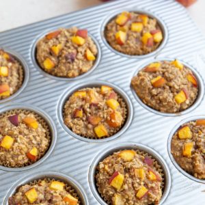 Muffin tray with peach muffins and fresh peaches to the side. Fresh out of the oven and ready to eat.