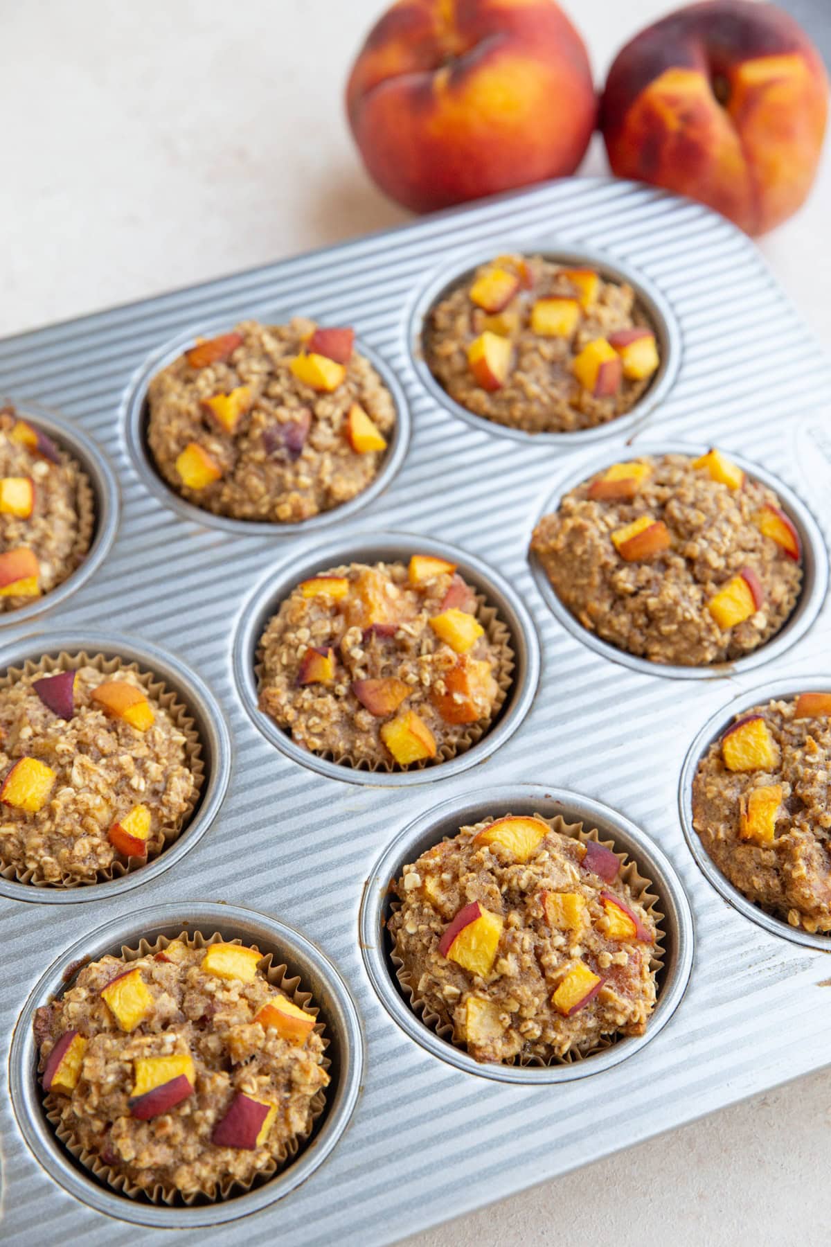 Muffin tray with peach muffins and fresh peaches to the side. Fresh out of the oven and ready to eat.