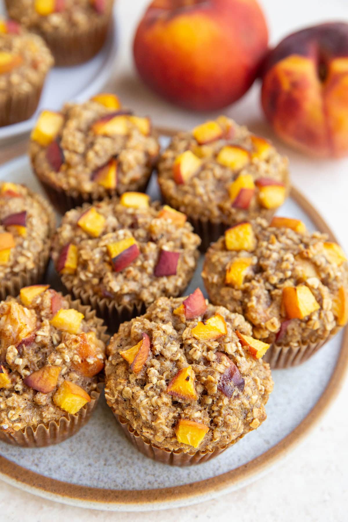 Plate of peach oatmeal muffins with fresh peaches in the background.