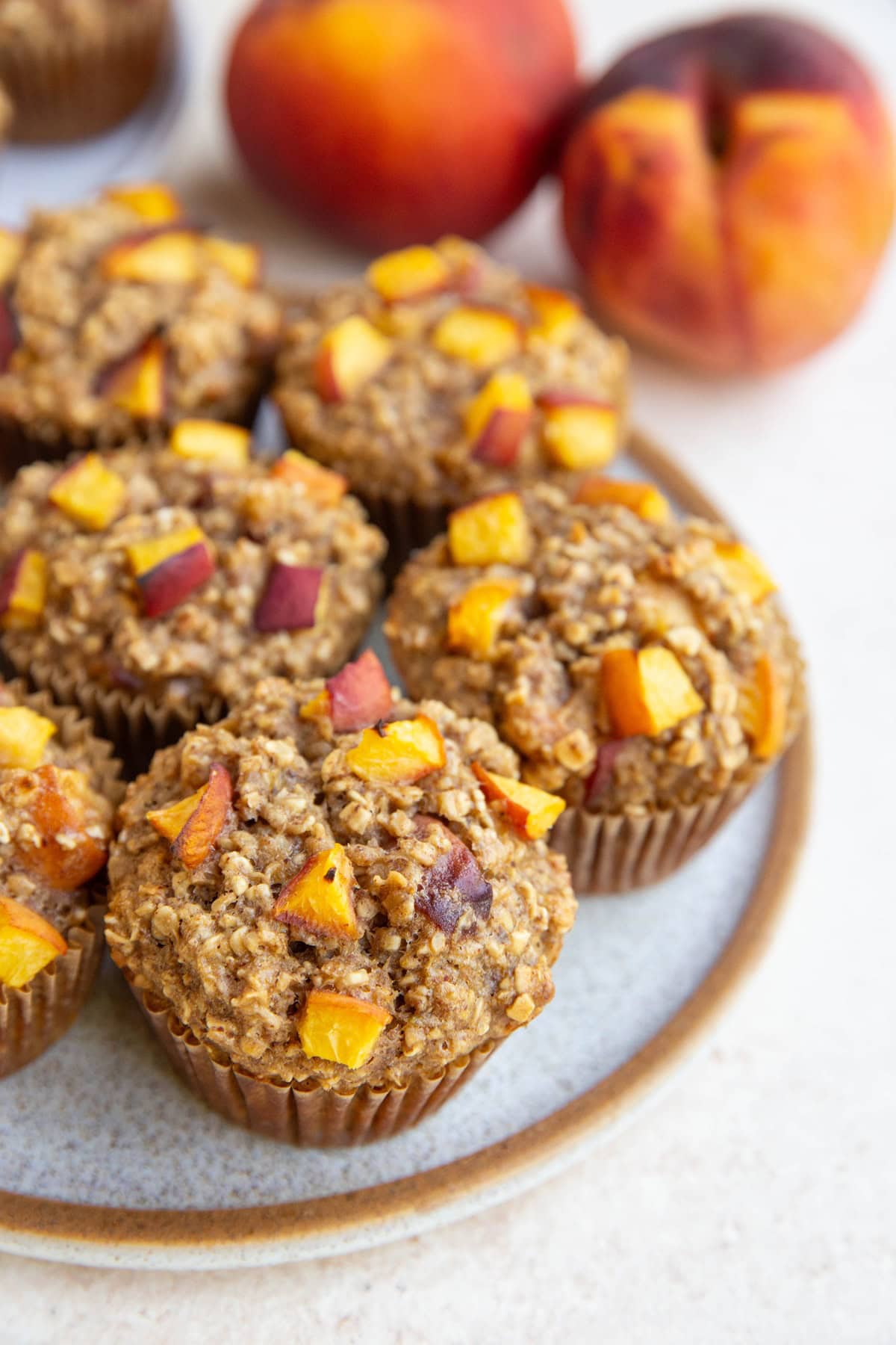 Plate of peach muffins with fresh peaches in the background.