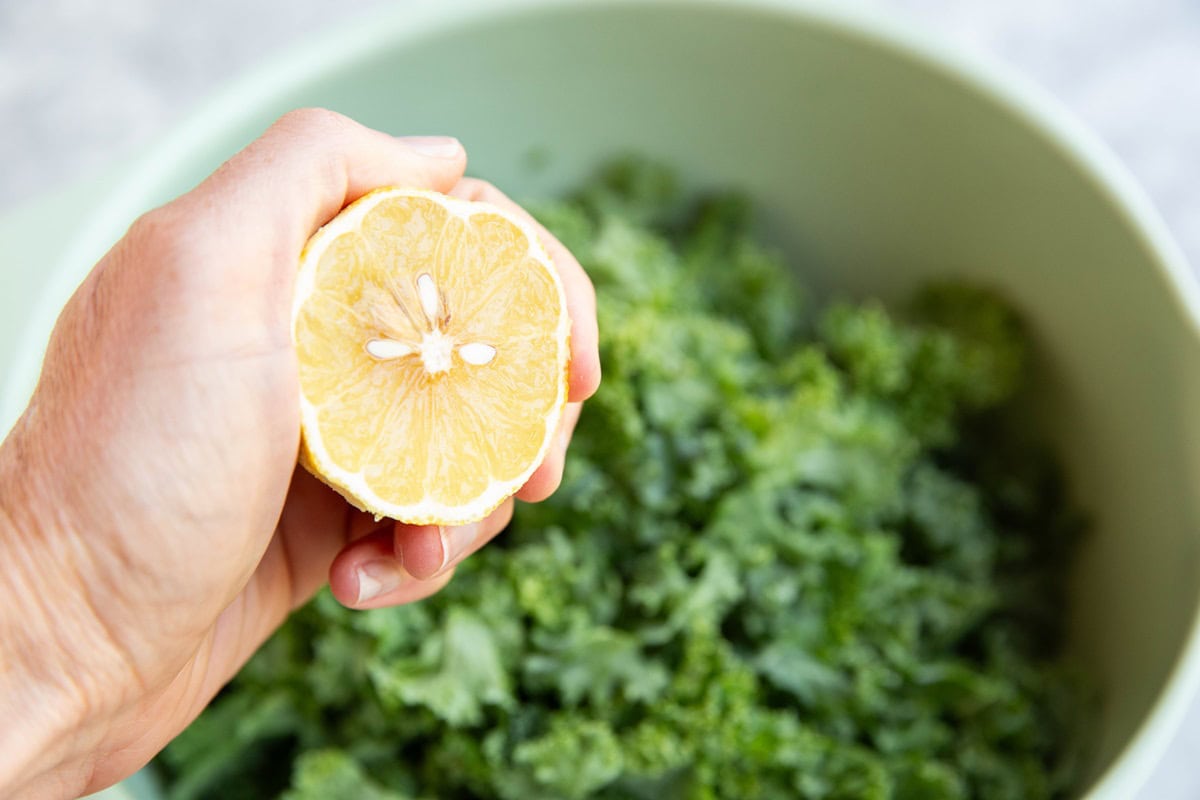 Hand squeezing a lemon into a bowl with chopped kale leaves.