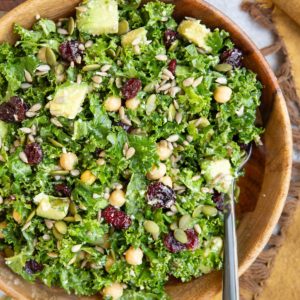 Wooden bowl full of kale salad with a fork and a golden napkin to the side, ready to eat.