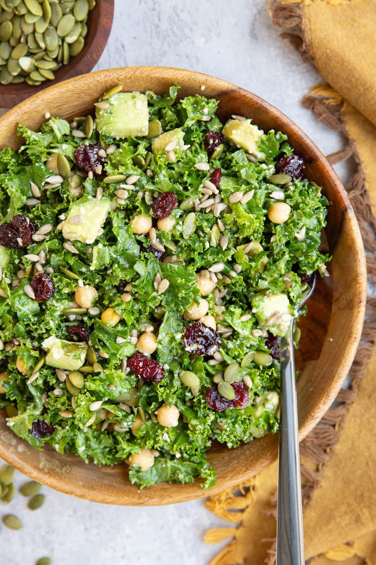 Wooden bowl full of kale salad with a fork and a golden napkin to the side, ready to eat.