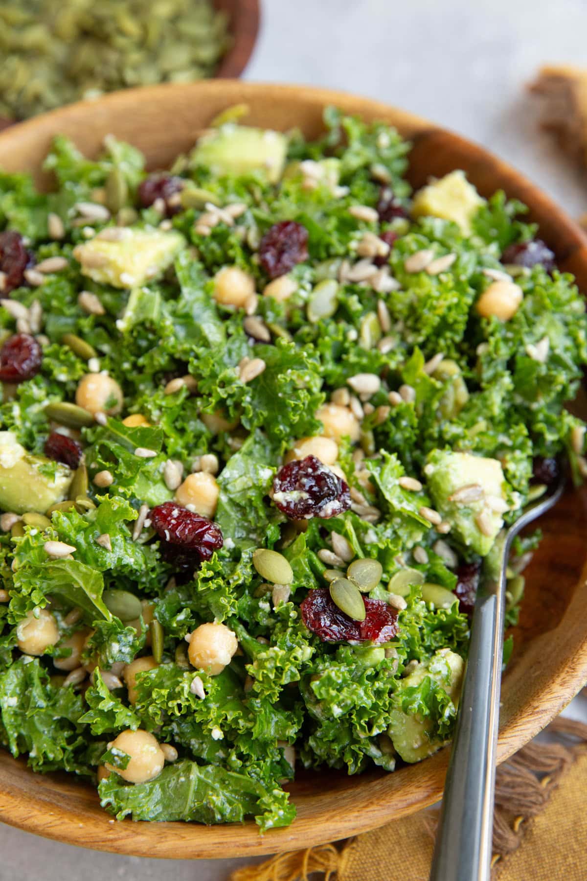 Big bowl of kale salad with a dork and pumpkin seeds in the background.