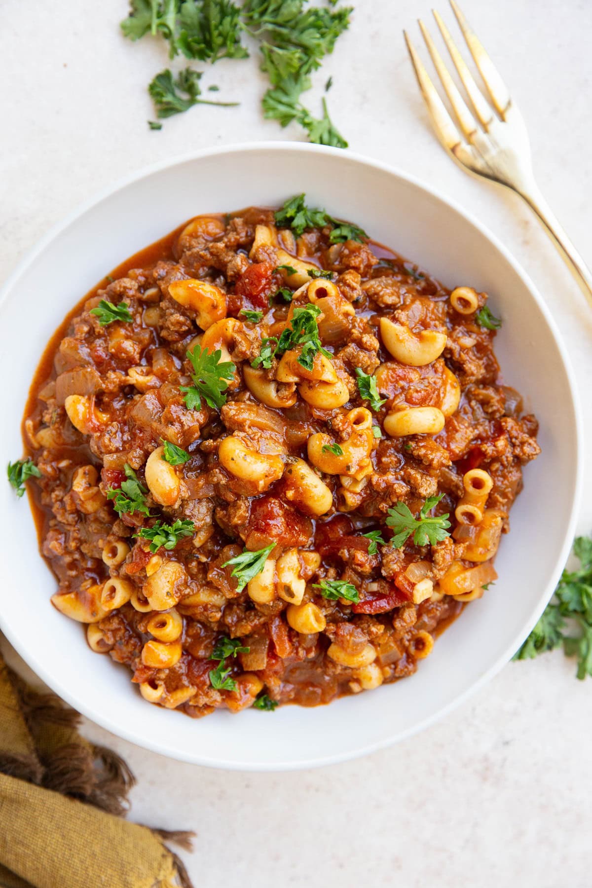 Bowl of American goulash with a gold fork to the side and fresh parlsey.