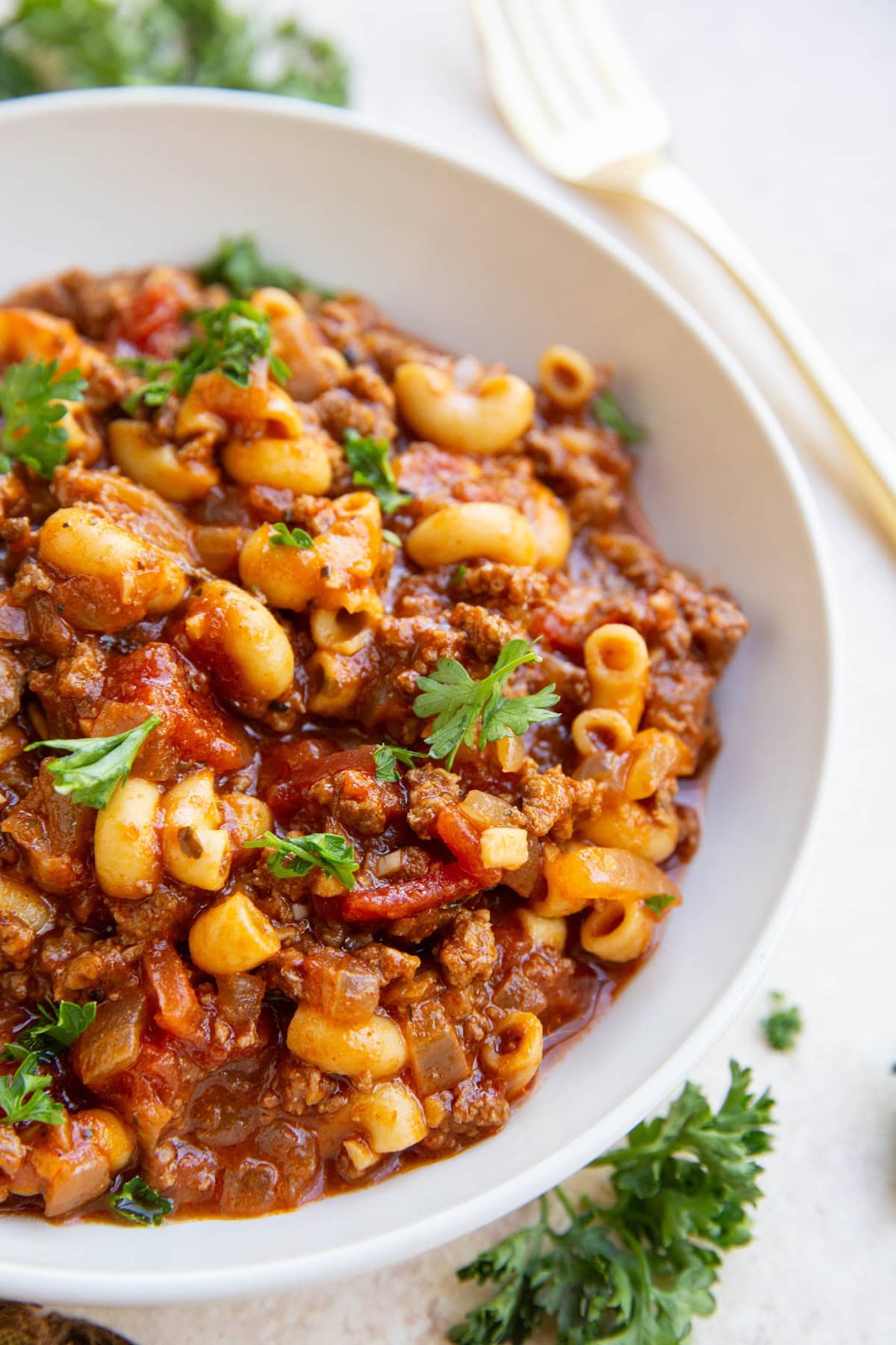 Big white bowl of goulash with a golden fork to the side and fresh parsley.