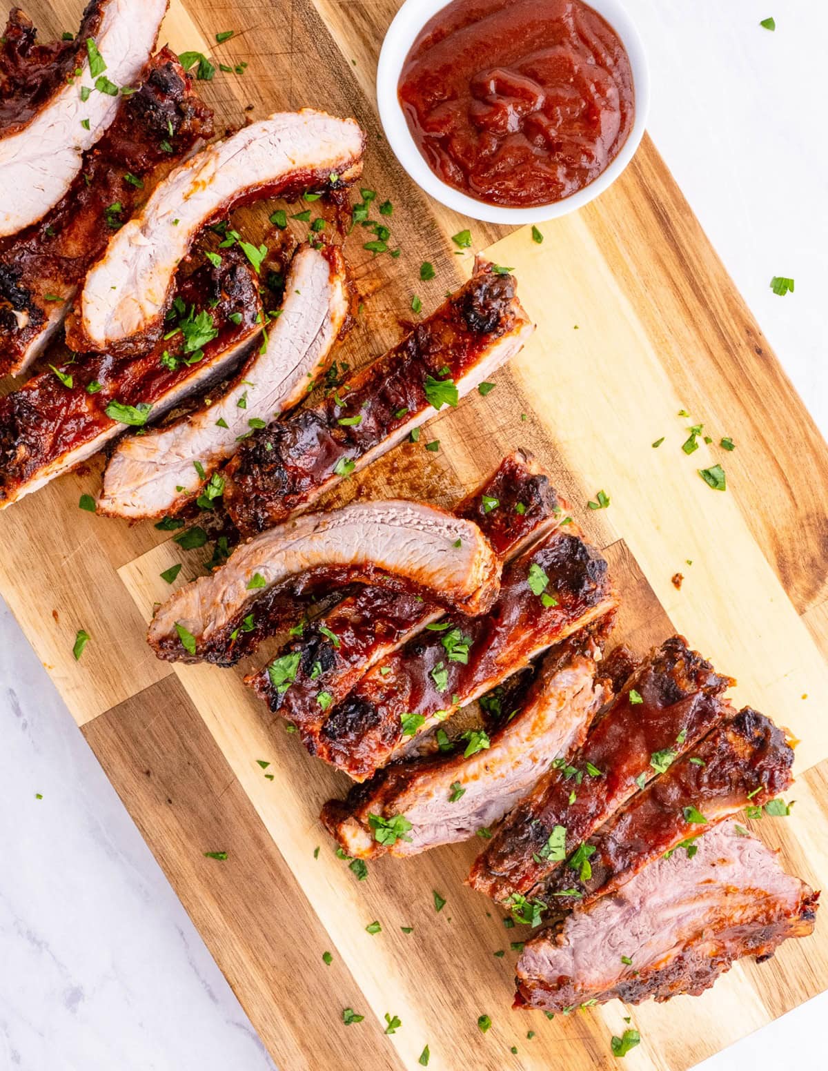 Wooden cutting board with a rack of ribs cut into individual ribs.