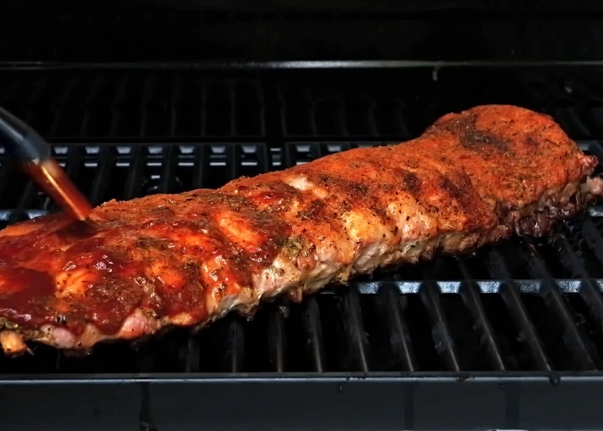 Brushing bbq sauce over the dry rub ribs.