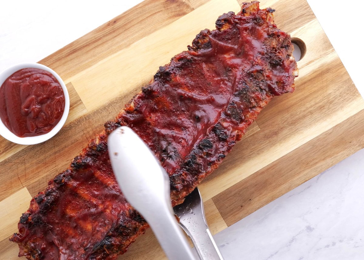 Tongs moving a rack of ribs to a cutting board.