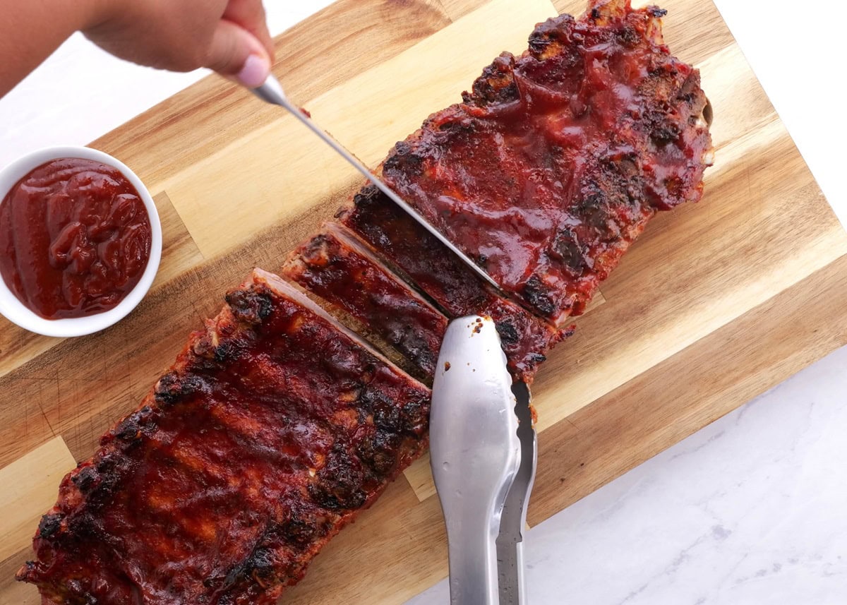 Slicing rack of ribs into individual bones using a knife and tongs.