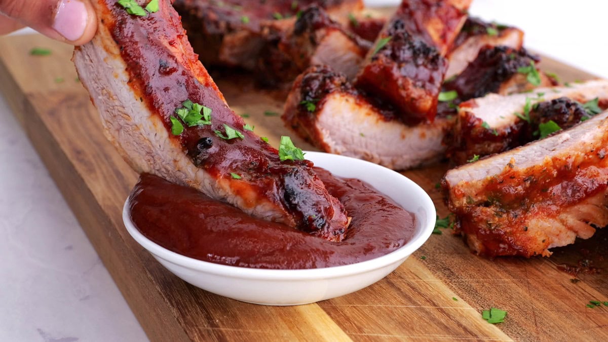 Hand dipping a rib into barbecue sauce, ready to eat.