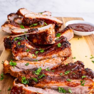 BBQ ribs cut up on a cutting board with bbq sauce and sprinkles of parsley