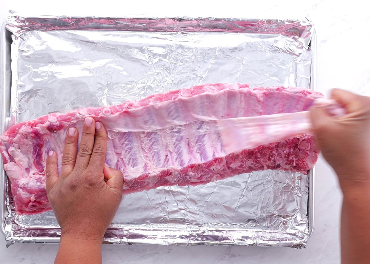 Hand pulling silver skin off of the back side of a rack of ribs.