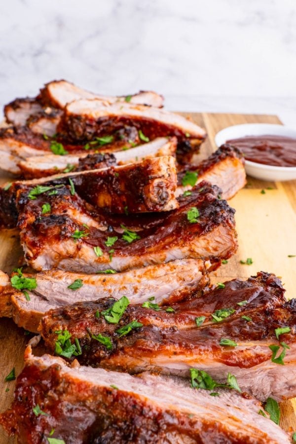 BBQ ribs cut up on a cutting board with bbq sauce and sprinkles of parsley