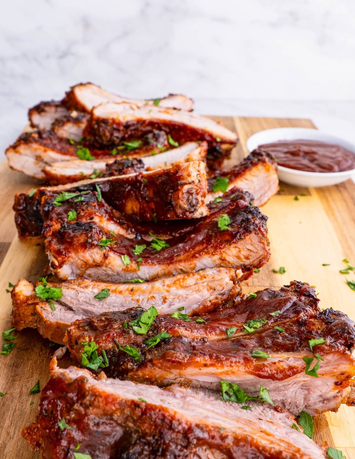 BBQ ribs cut up on a cutting board with bbq sauce and sprinkles of parsley