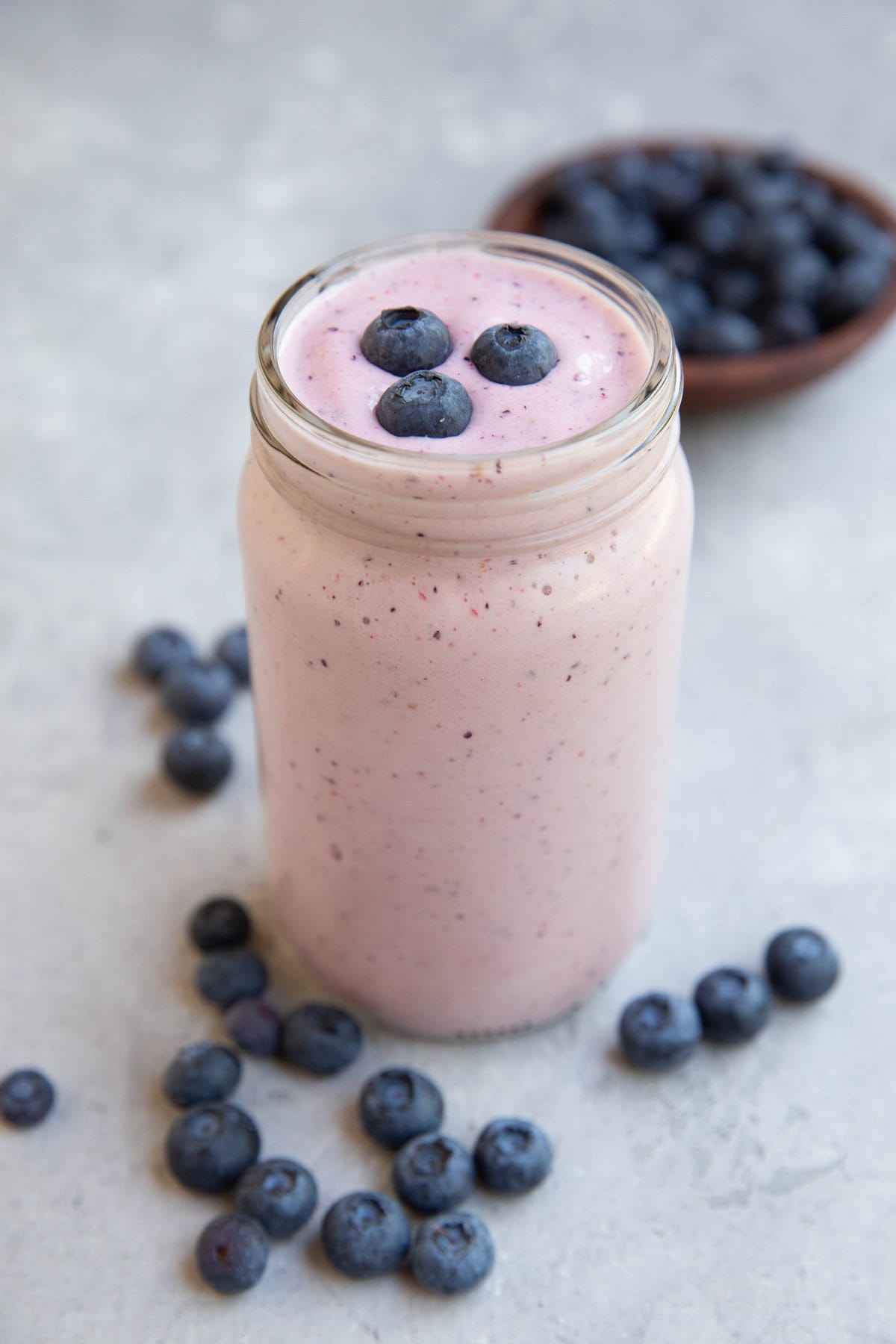 Glass jar with berry protein smoothie with fresh berries on top of the smoothie.