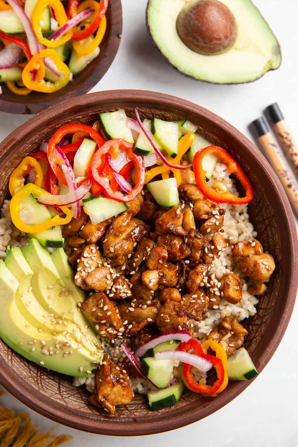 Ceramic bowl full of rice, chicken, pickled vegetables, and avocado slices.