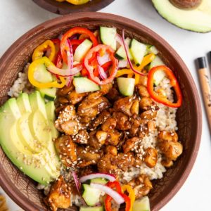 Chicken and rice bowl with pickled vegetables and avocado with a bowl of pickled veggies to the side and chop sticks.