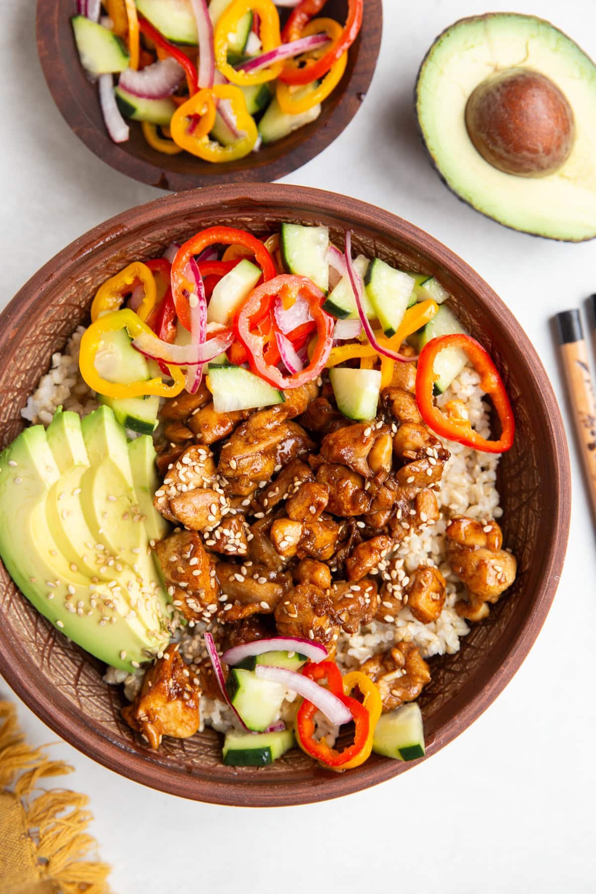 Chicken and rice bowl with pickled vegetables and avocado with a bowl of pickled veggies to the side and chop sticks.