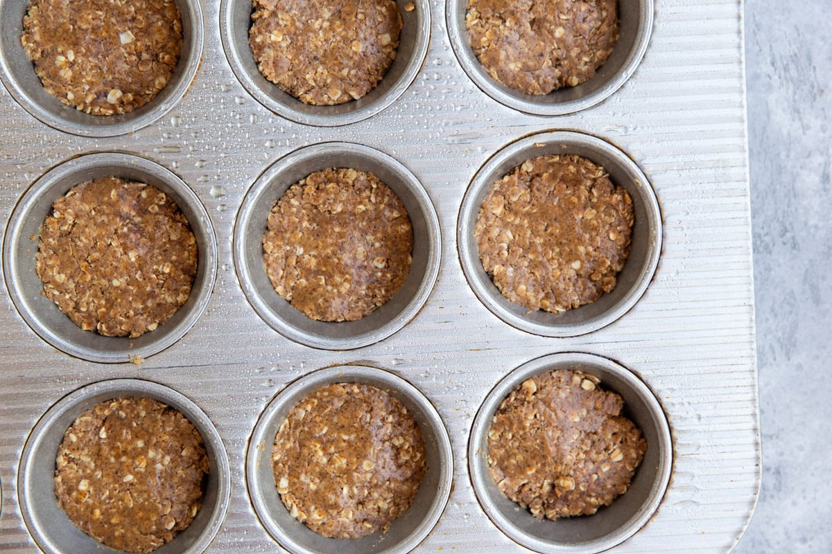 Muffin tray with almond butter oatmeal mixture pressed into an even layer to make almond butter cups.