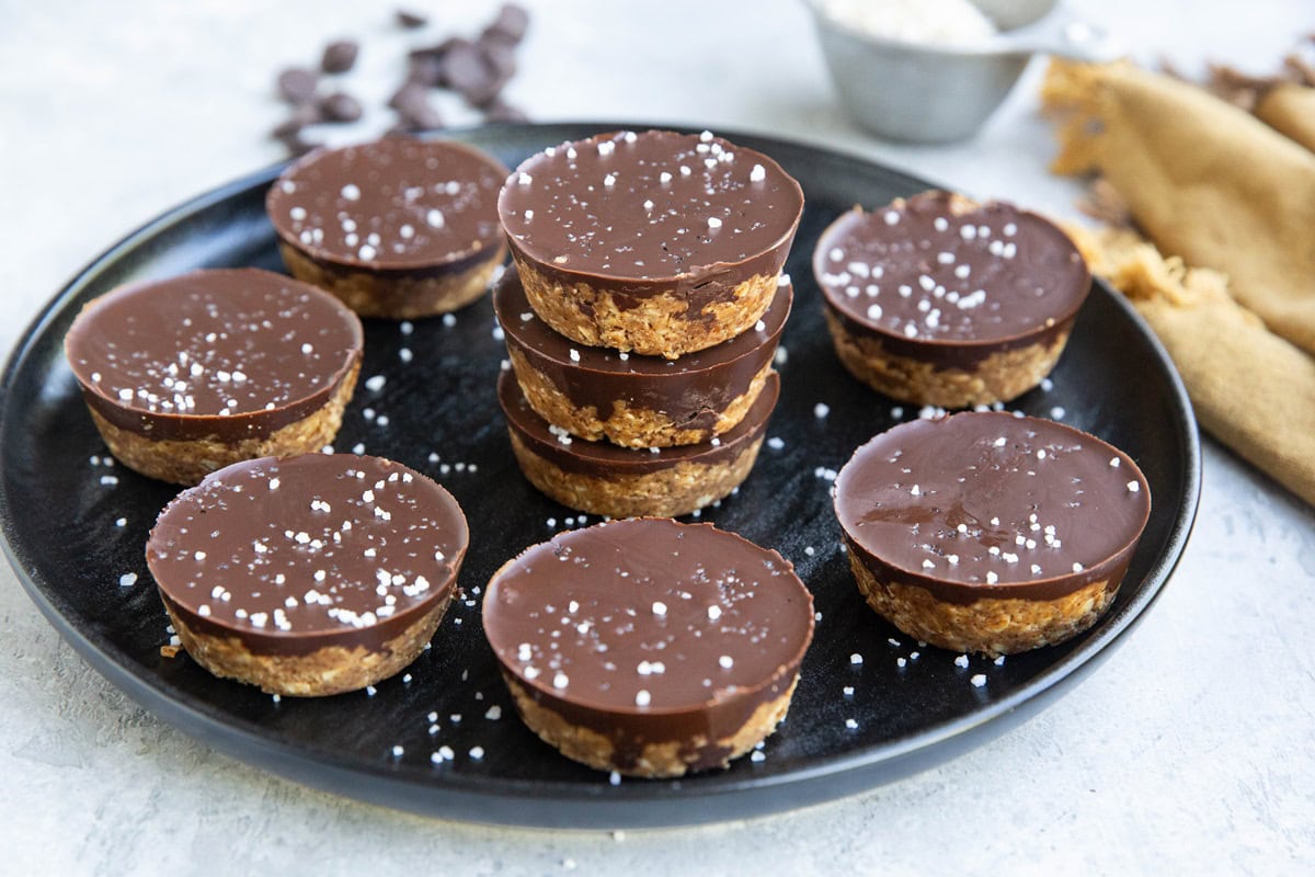 Black plate with finished no-bake almond butter cups sitting on it, ready to eat.