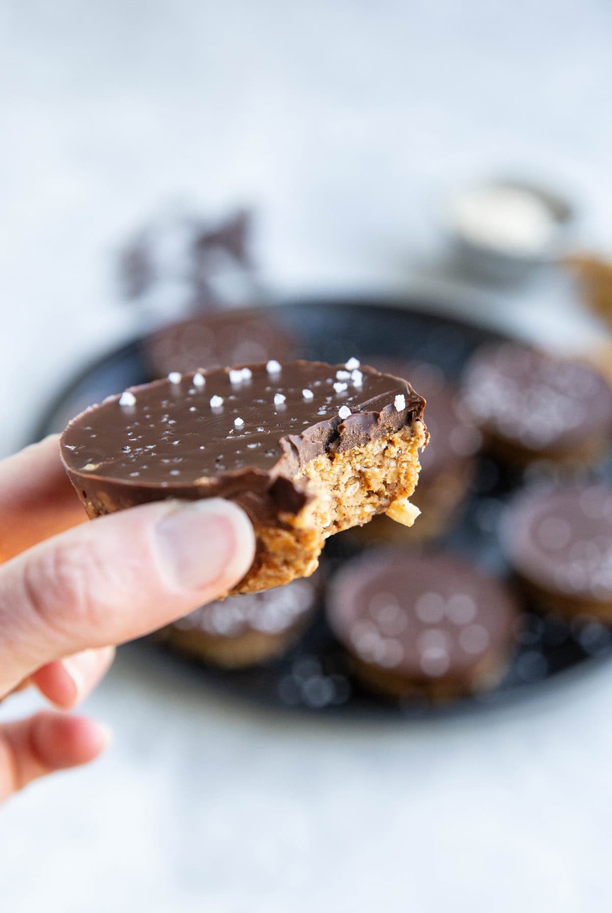 Hand holding an almond butter cup with a bite taken out.