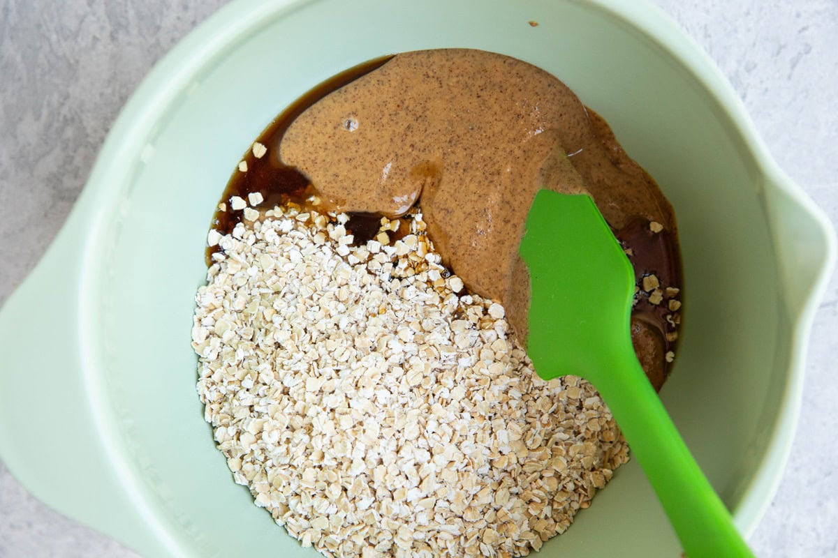 Mixing bowl full of almond butter, pure maple syrup, and oats, ready to be mixed together.