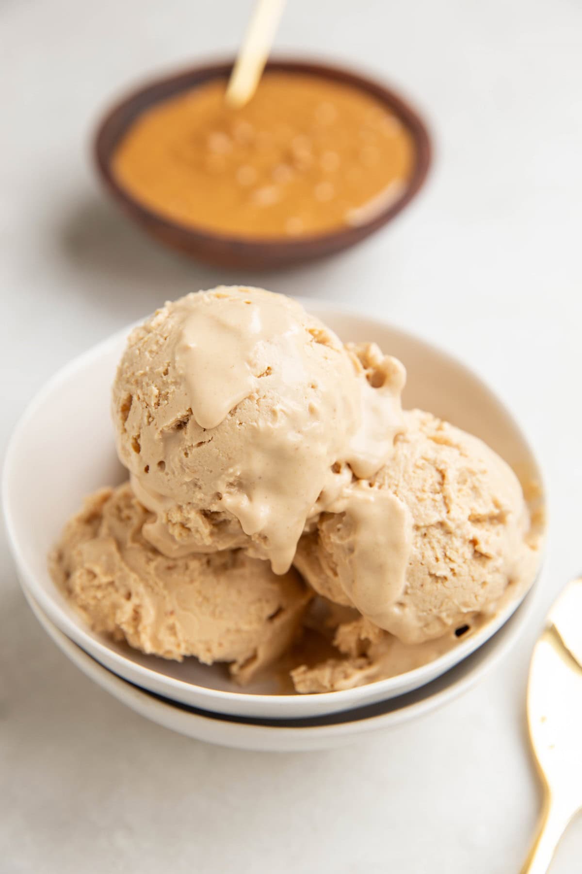 Small white bowl with a few scoops of peanut butter frozen yogurt inside and a bowl of peanut butter in the background.