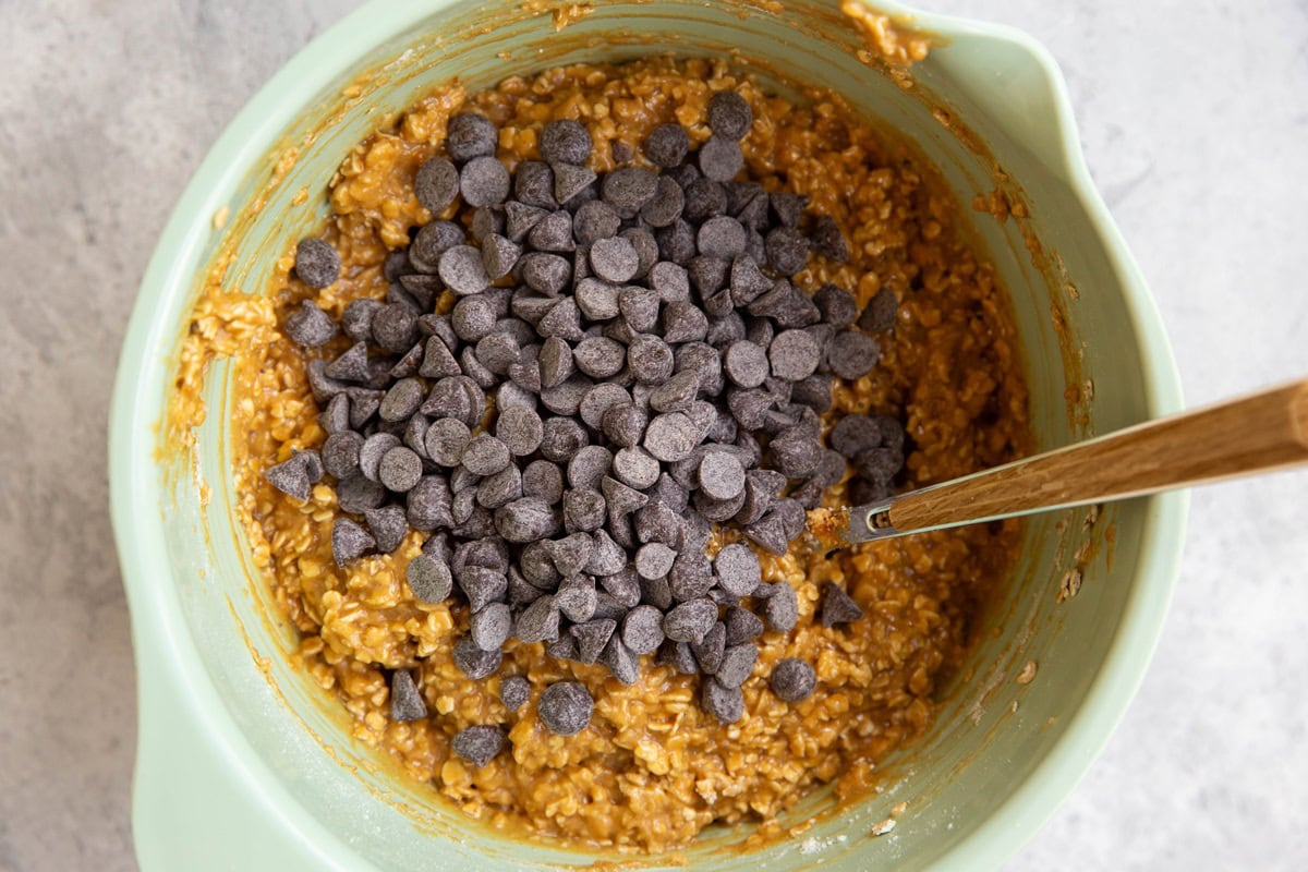 Chocolate chips on top of peanut butter cookie dough, ready to be mixed in.