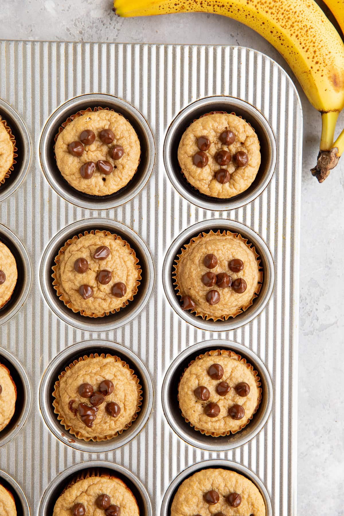 Muffin tray of protein muffins, fresh out of the oven with a ripe banana to the side.