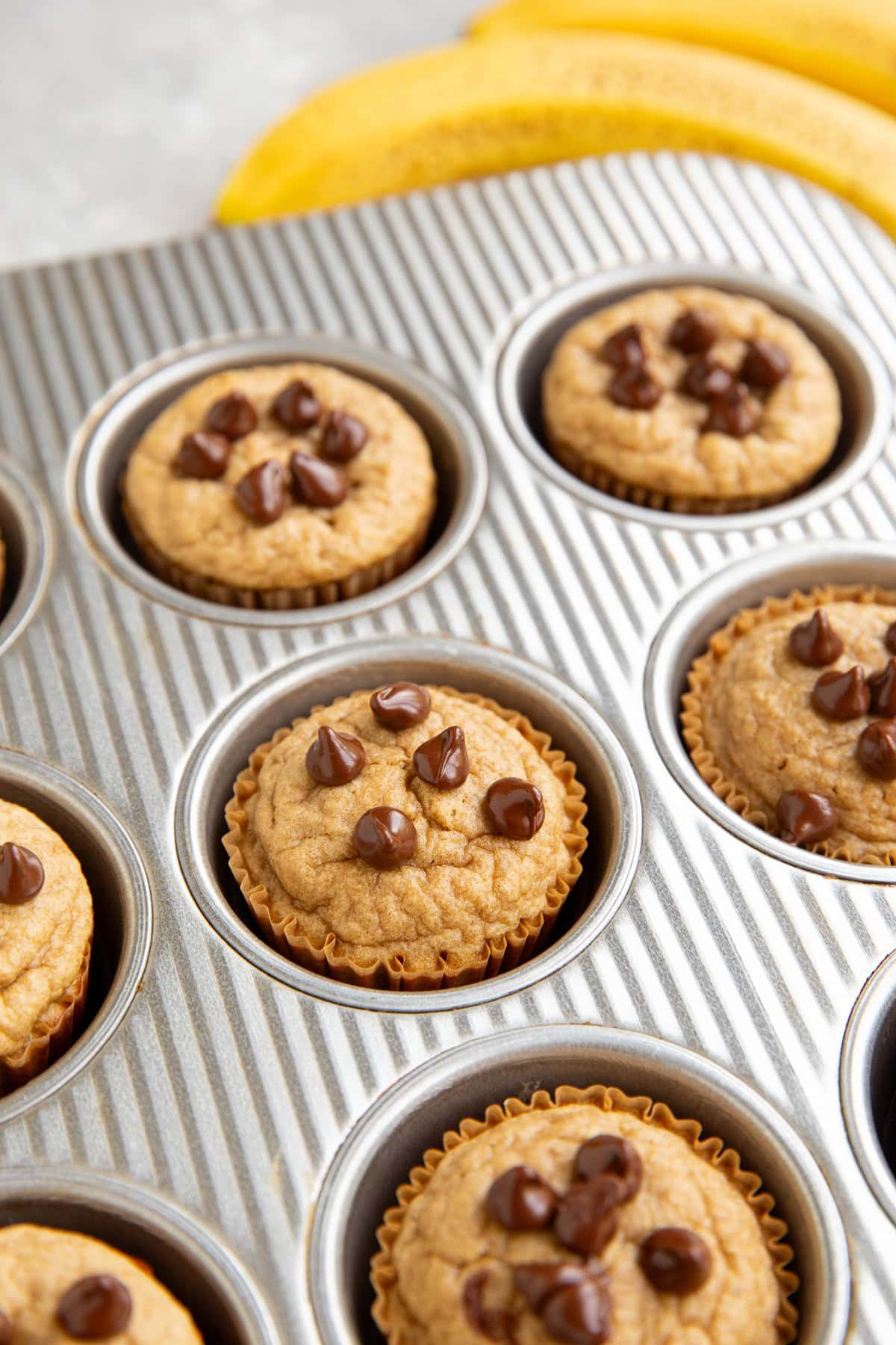 Muffin pan with banana protein muffins, fresh out of the oven with ripe bananas to the side.