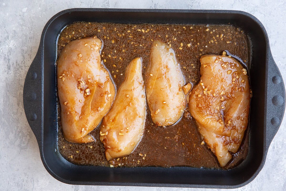 Raw chicken breasts in a large casserole dish with marinade, ready to go into the oven.