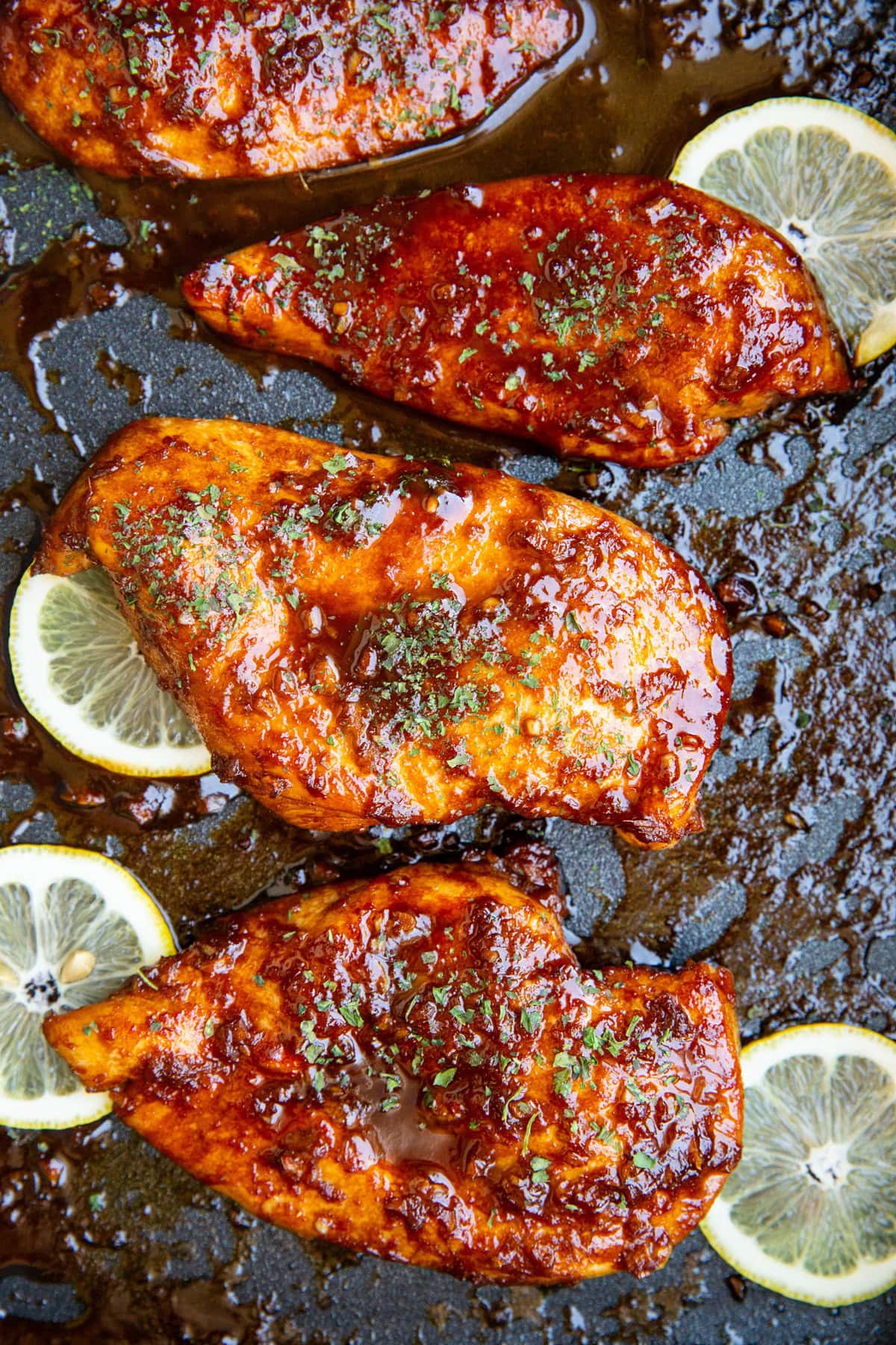 Sesame garlic ginger chicken fresh out of the oven in a casserole dish with lemon slices and a sprinkle of dried parsley.