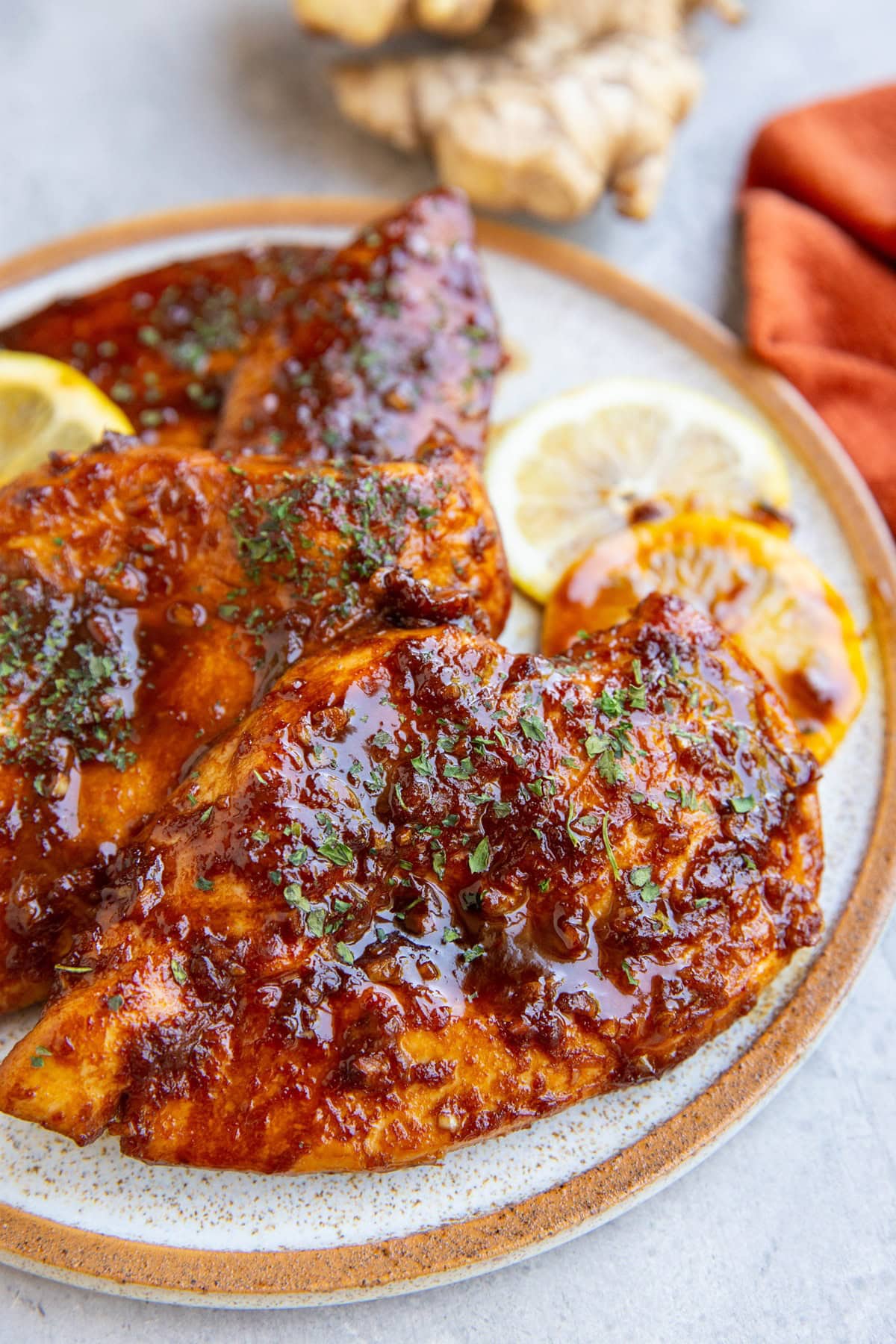 Sesame garlic ginger chicken on a plate with lemon slices and fresh ginger in the background, ready to eat.