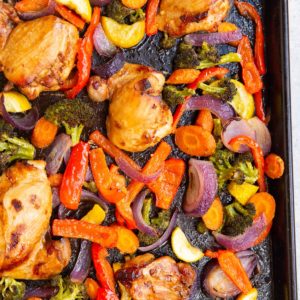 Rimmed sheet pan with roasted vegetables and chicken thighs. Fresh out of the oven and ready to serve.