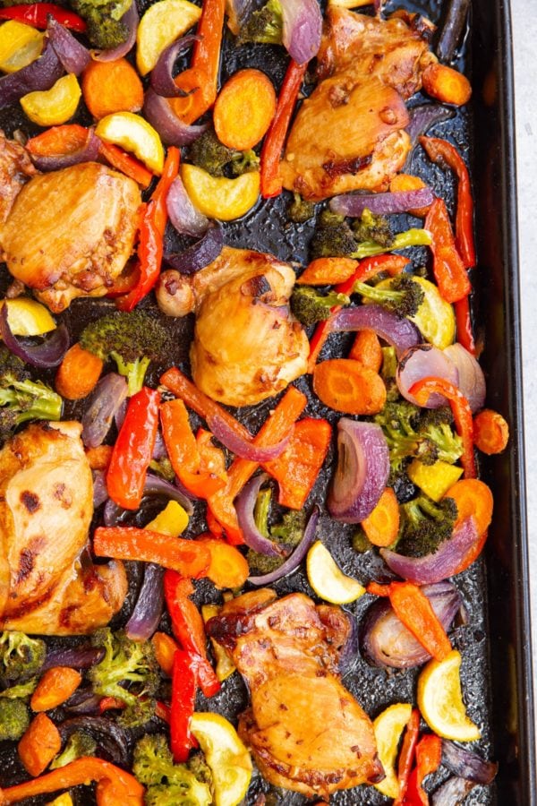 Rimmed sheet pan with roasted vegetables and chicken thighs. Fresh out of the oven and ready to serve.